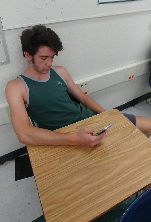 Photo illustration of student using his phone wasting valuable class time; an epidemic among classrooms.