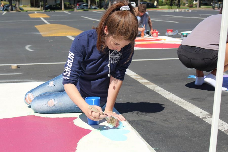 Senior Ellie Carey adds detail to her flower themed parking spot as her classmates work on theirs. Parking lot painting day was Sept. 24. In total, 86 spots were purchased.